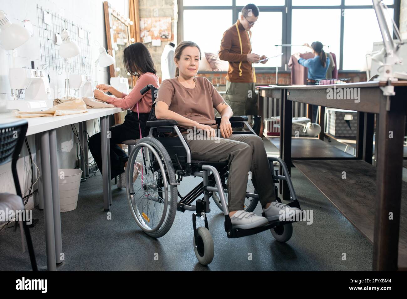 Buon sarto in sedia a rotelle che guarda contro i colleghi che lavorano Foto Stock