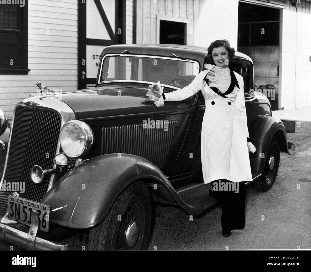 L'attrice americana Myrna Loy (Myrna Adele Williams; 1905 - 1993) vestita in un abito da 'The Thin Man', si trova accanto ad un'auto in uno studio cinematografico, circa 1934. (Foto di Burton Holmes) Foto Stock