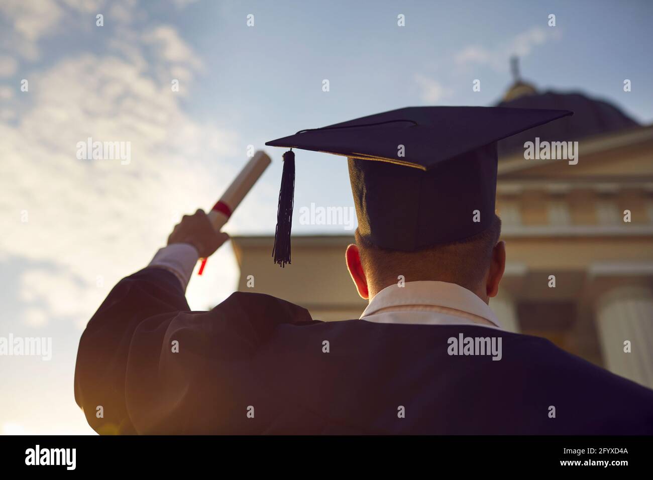 Studente di laurea in abiti tradizionali e cappello in piedi con rialzato diploma Foto Stock
