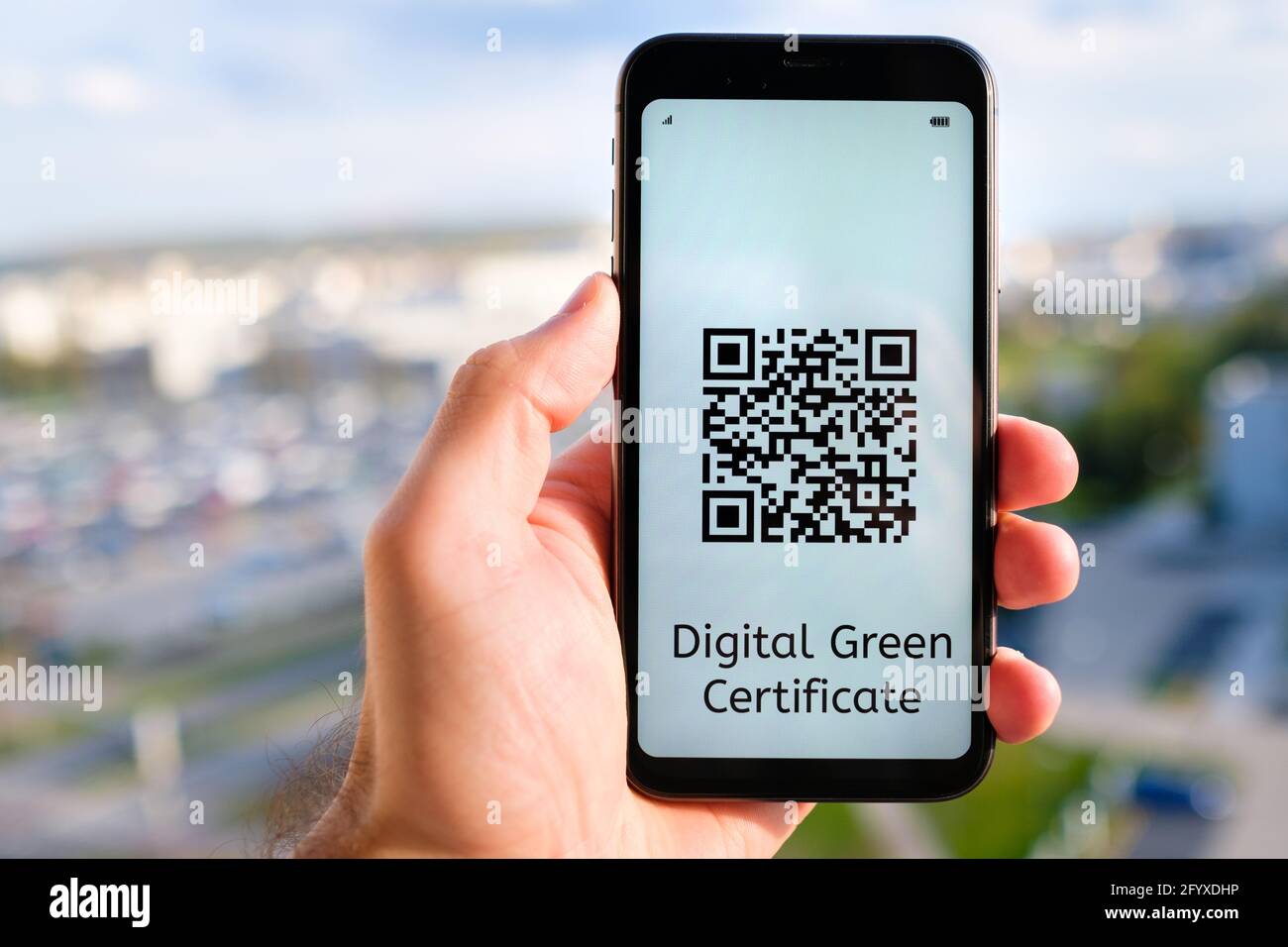 Certificato Verde digitale con codice QR sullo schermo del telefono cellulare in mano mans sullo sfondo del paesaggio urbano. Foto Stock