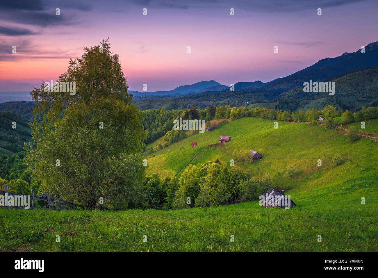 Maestoso paesaggio rurale con prati verdi e capanne in legno sulle pendici al tramonto, Simon, Romania, Europa Foto Stock