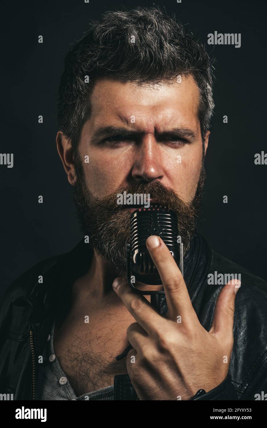 Voce maschile che canta in microfono in studio di registrazione. Bell'uomo con bearded in giacca di pelle con microfono. Musica rock. Cantante karaoke. Foto Stock