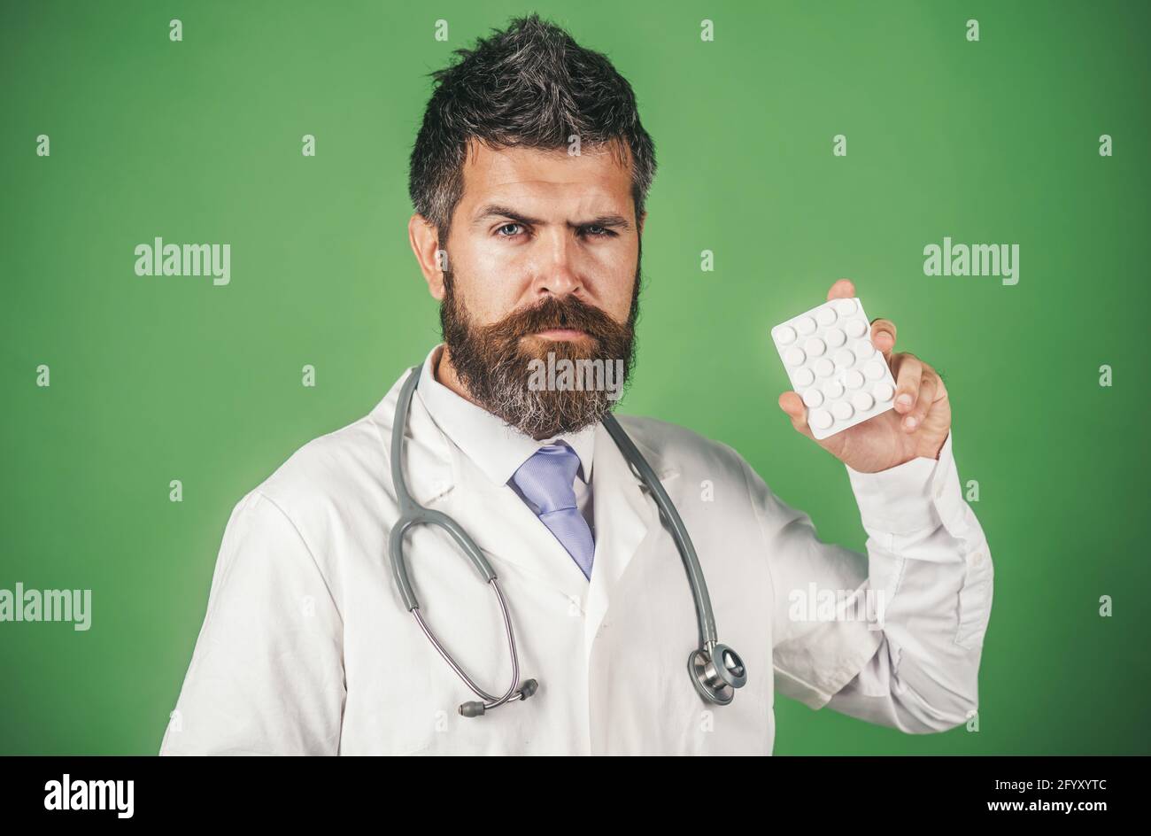 Medico serio in abito medico bianco con stetoscopio tiene le pillole in mano. Concetto di farmacia, medicina e assistenza sanitaria. Foto Stock
