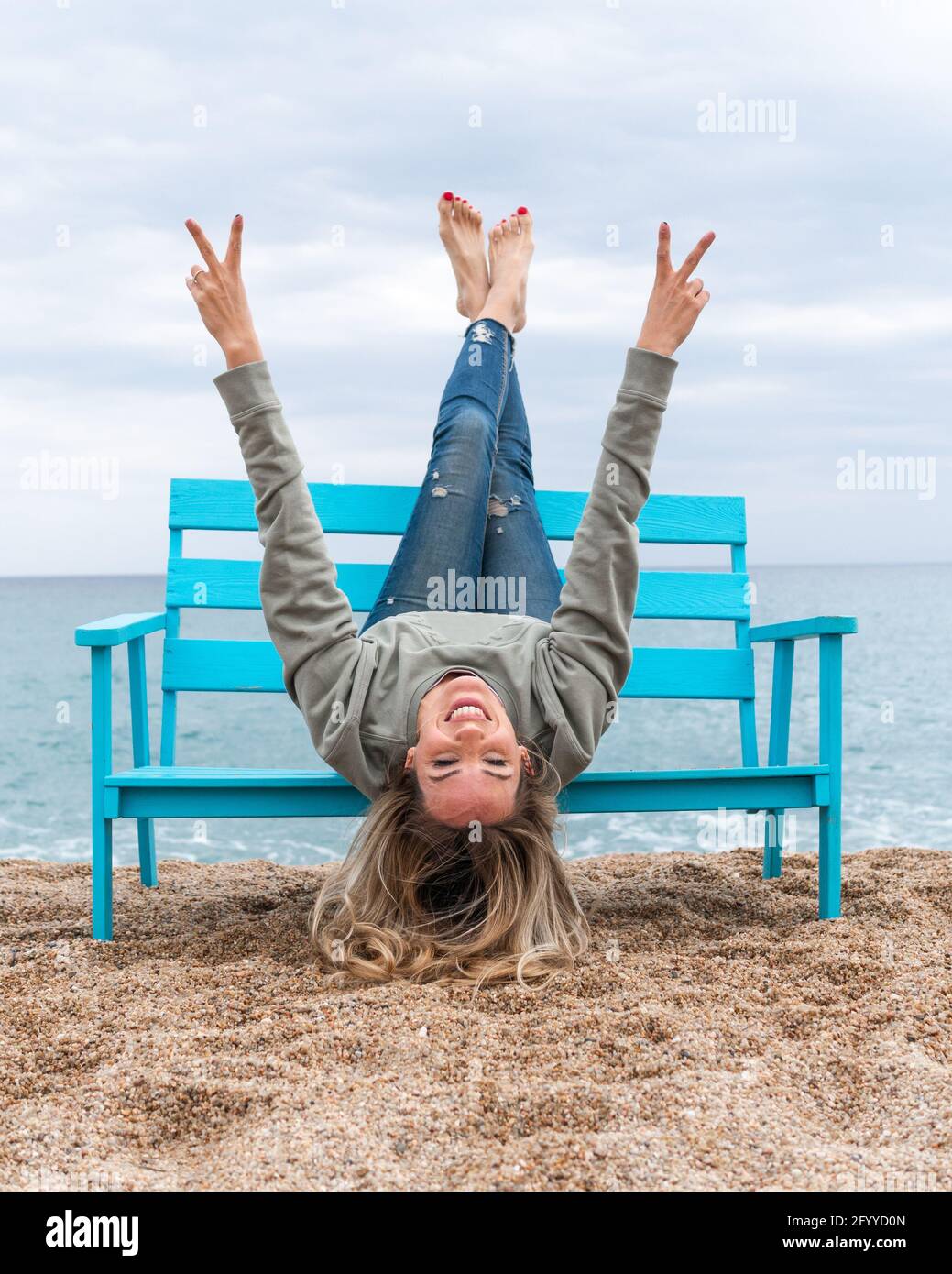 Donna allegra con gambe rialzate che mostrano un gesto di pace mentre si guarda con la fotocamera sulla costa dell'oceano Foto Stock