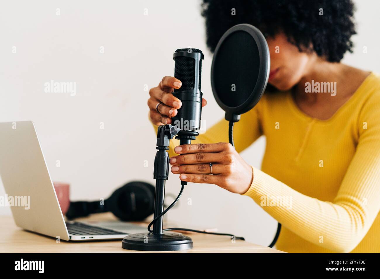 Crop Unriconoscable African American femmina musicista con capelli scuri ricci impostare il microfono prima di registrare la canzone in studio luce Foto Stock