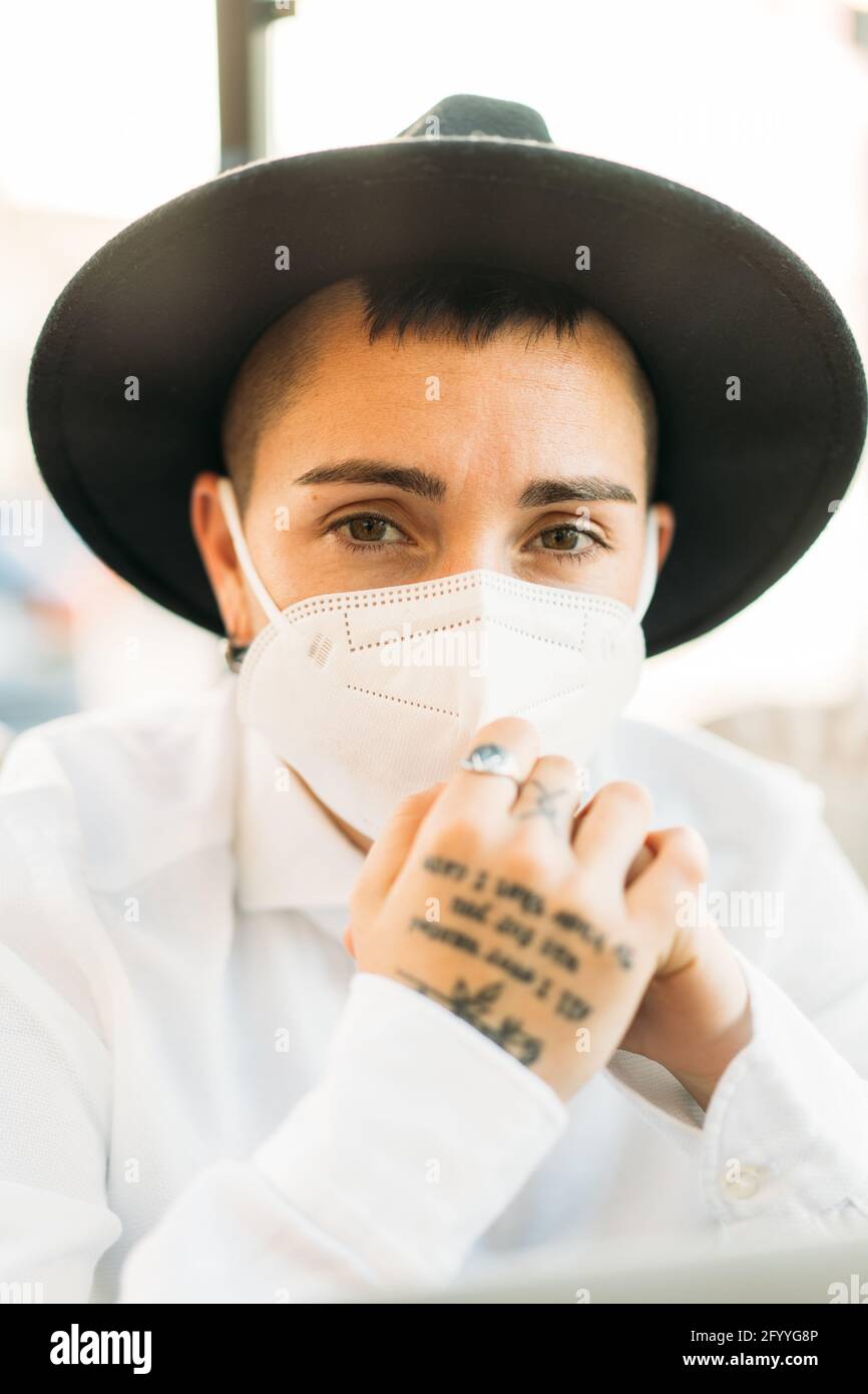 Donna maschile con tatuaggi sulle mani in cappello con maschera medica e cappello elegante Foto Stock