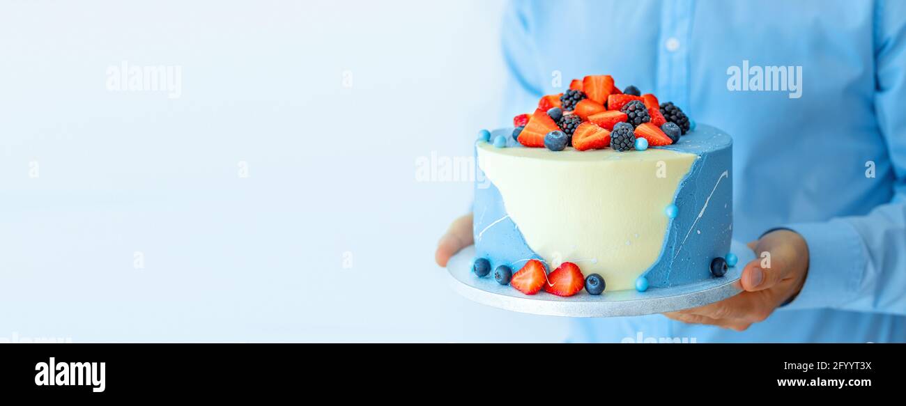 Un uomo pasticceria shef tenendo una bella torta grande con frutti di bosco in mano. Chef maschile cuoco confettiere o panettiere. Simulazione del concetto di cibo di spazio di copia Foto Stock