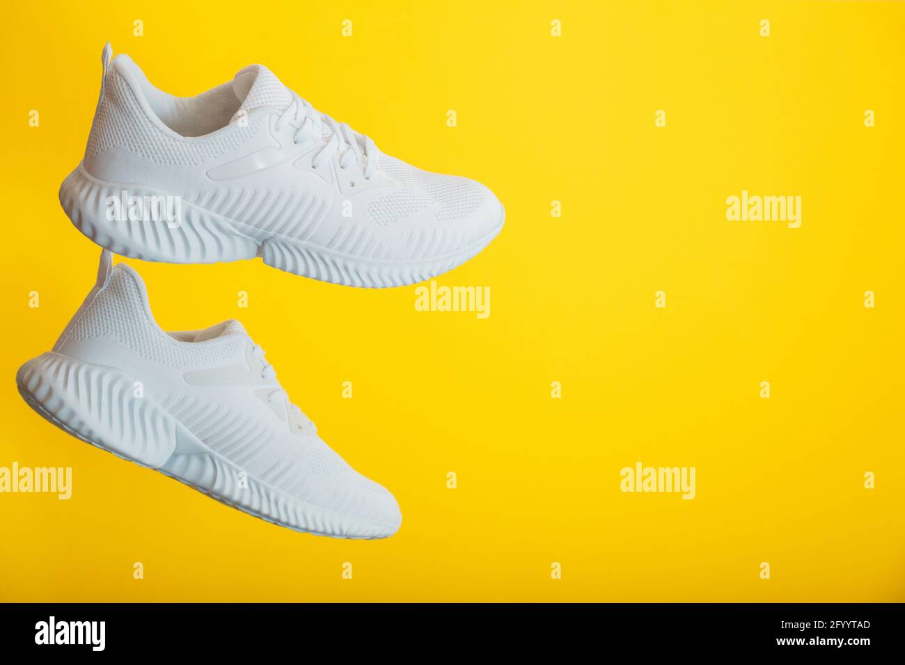 Le scarpe da ginnastica bianche volano su sfondo giallo. Coppia di moderne sneakers bianche maschili di sport da jogging sulla parete a colori con spazio di copia. Foto Stock