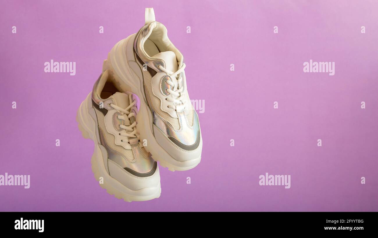 Le sneakers bianche volano sulla parete viola. Scarpe donna in pelle bianca su sfondo viola. Un paio di eleganti sneaker urbane. Comodo hipster sportivo Foto Stock