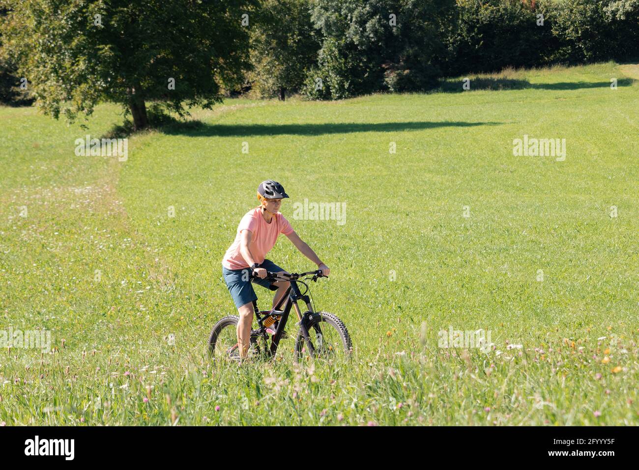 Donna in mountain bike su un prato verde in estate. Foto Stock