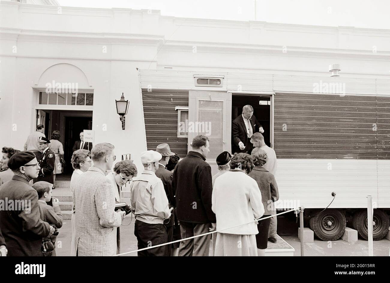 I visitatori aspettano in fila fuori da un rimorchio allestito vicino all'ingresso dell'ala est della Casa Bianca per lasciare le loro telecamere, borse e pacchi per l'ispezione, come parte delle nuove precauzioni di sicurezza stabilite in risposta alla crisi a Cuba. Washington, D.C. 23 ottobre 1962 Foto Stock