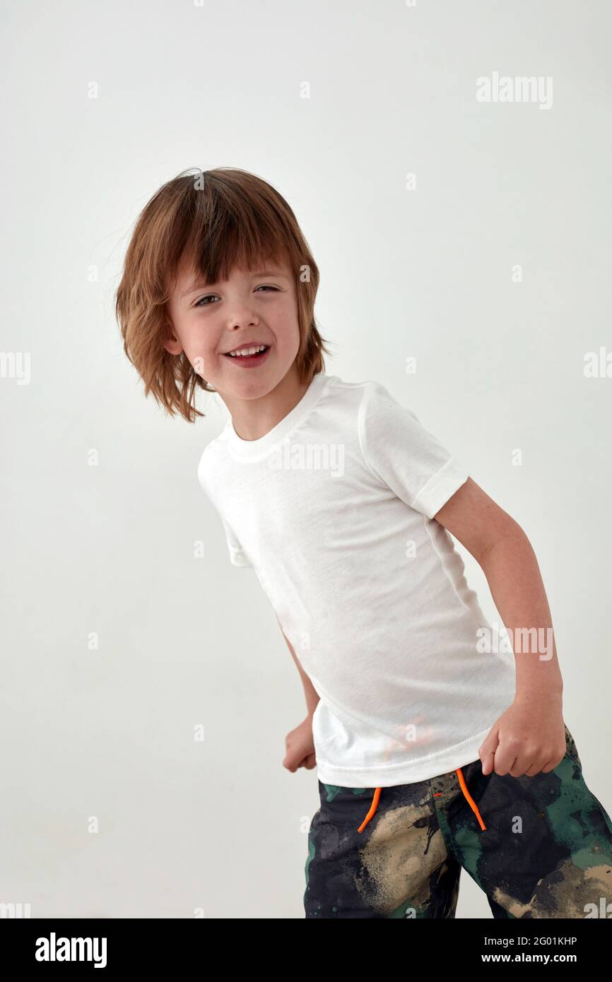 Happy boy in una t-shirt bianca casual in piedi contro il bianco parete e guardando la fotocamera Foto Stock