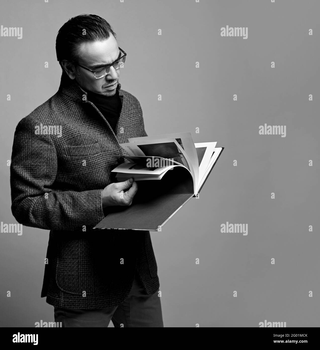 Ritratto in bianco e nero di un uomo di stile critico letterario in giacca a scacchi e sciarpa nera guardando attraverso il nuovo libro Foto Stock