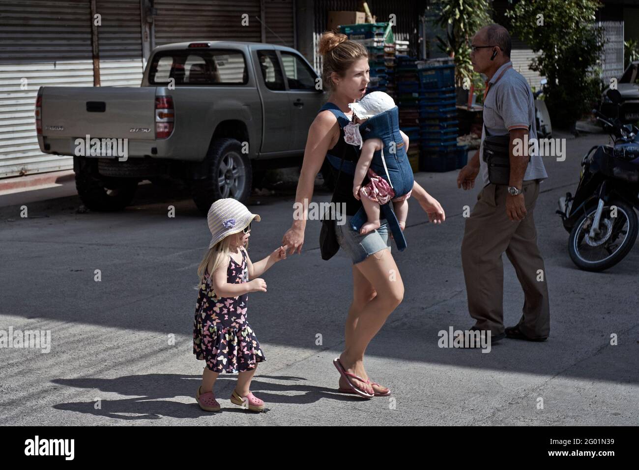 Madre che trasporta il bambino nell'imbragatura anteriore del supporto del bambino mentre prende bambini che camminano all'aperto Foto Stock