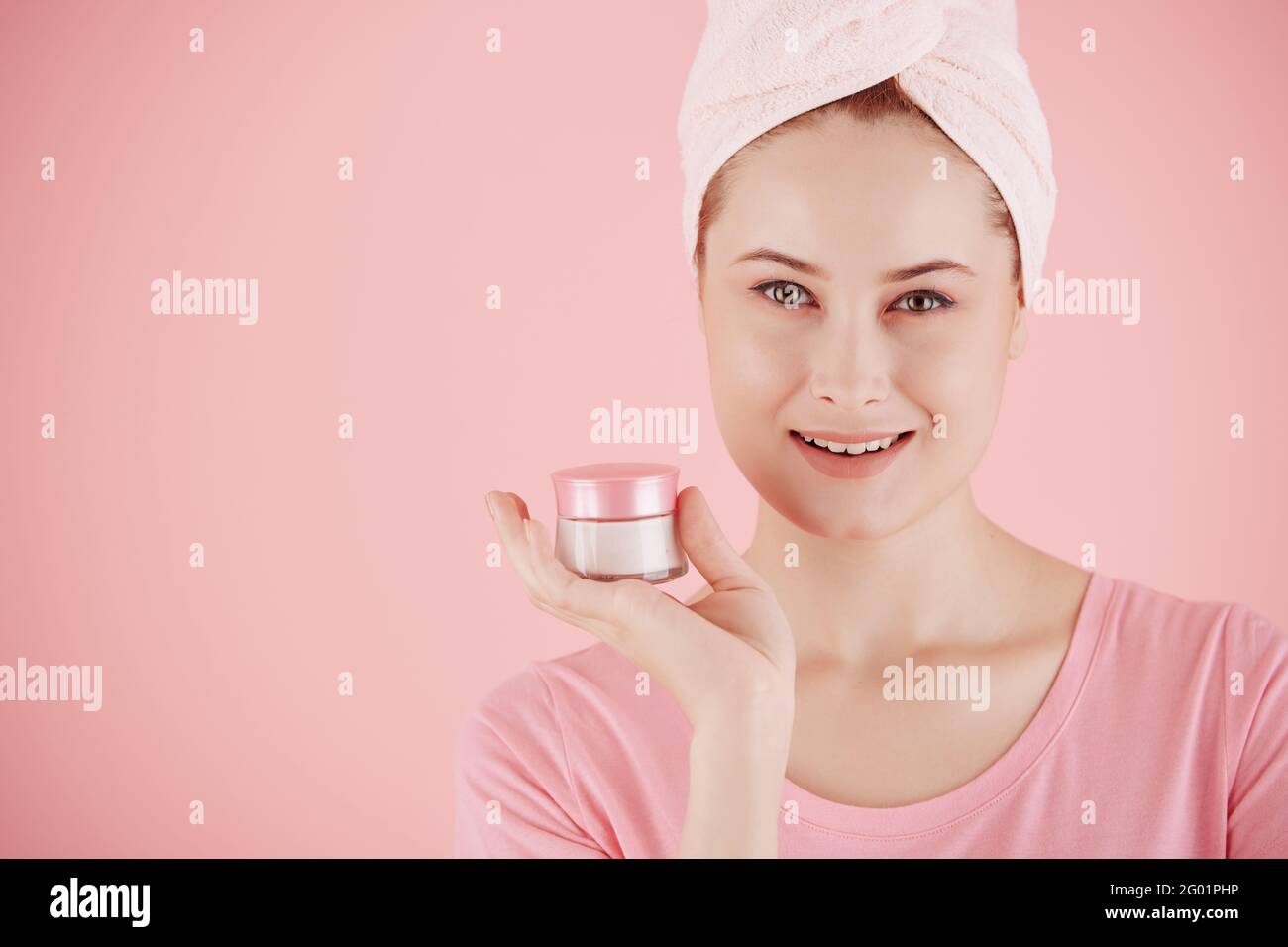 Bella giovane donna sorridente con asciugamano capelli che tiene il vaso di crema viso notte anti-invecchiamento Foto Stock