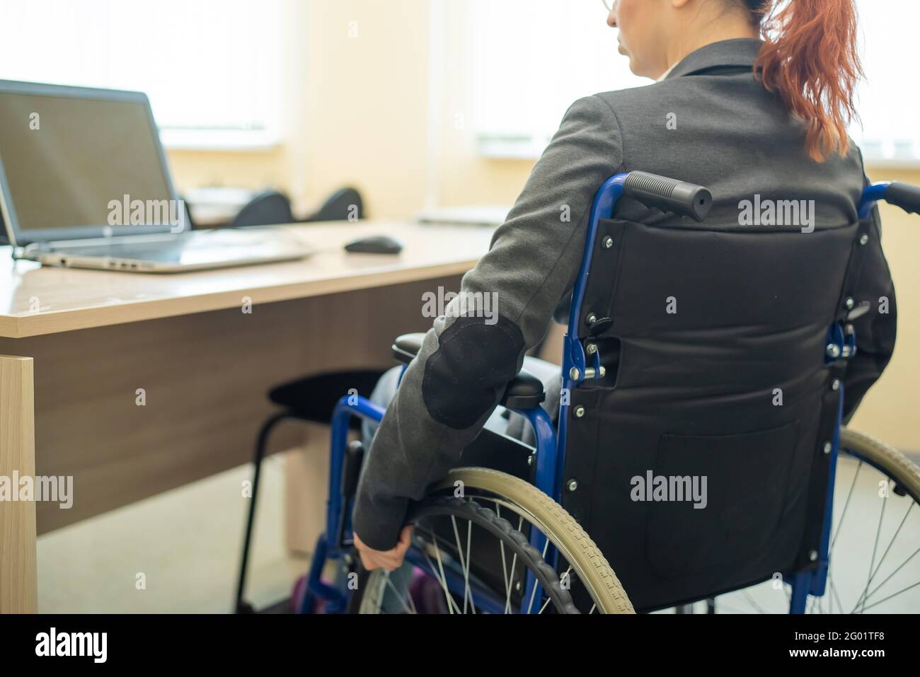 Giovane donna lavora su un computer portatile mentre si siede in una sedia a rotelle in una sala conferenze universitaria. Condizioni per l'insegnamento di una persona disabile Foto Stock