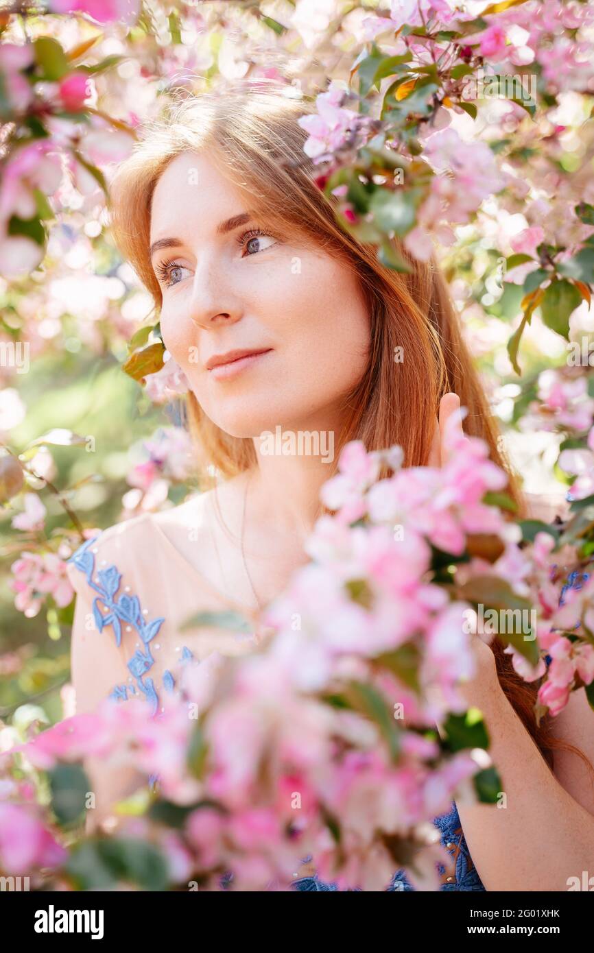 Ritratto di una ragazza dai capelli rossi su uno sfondo di fiori rosa. Foto Stock