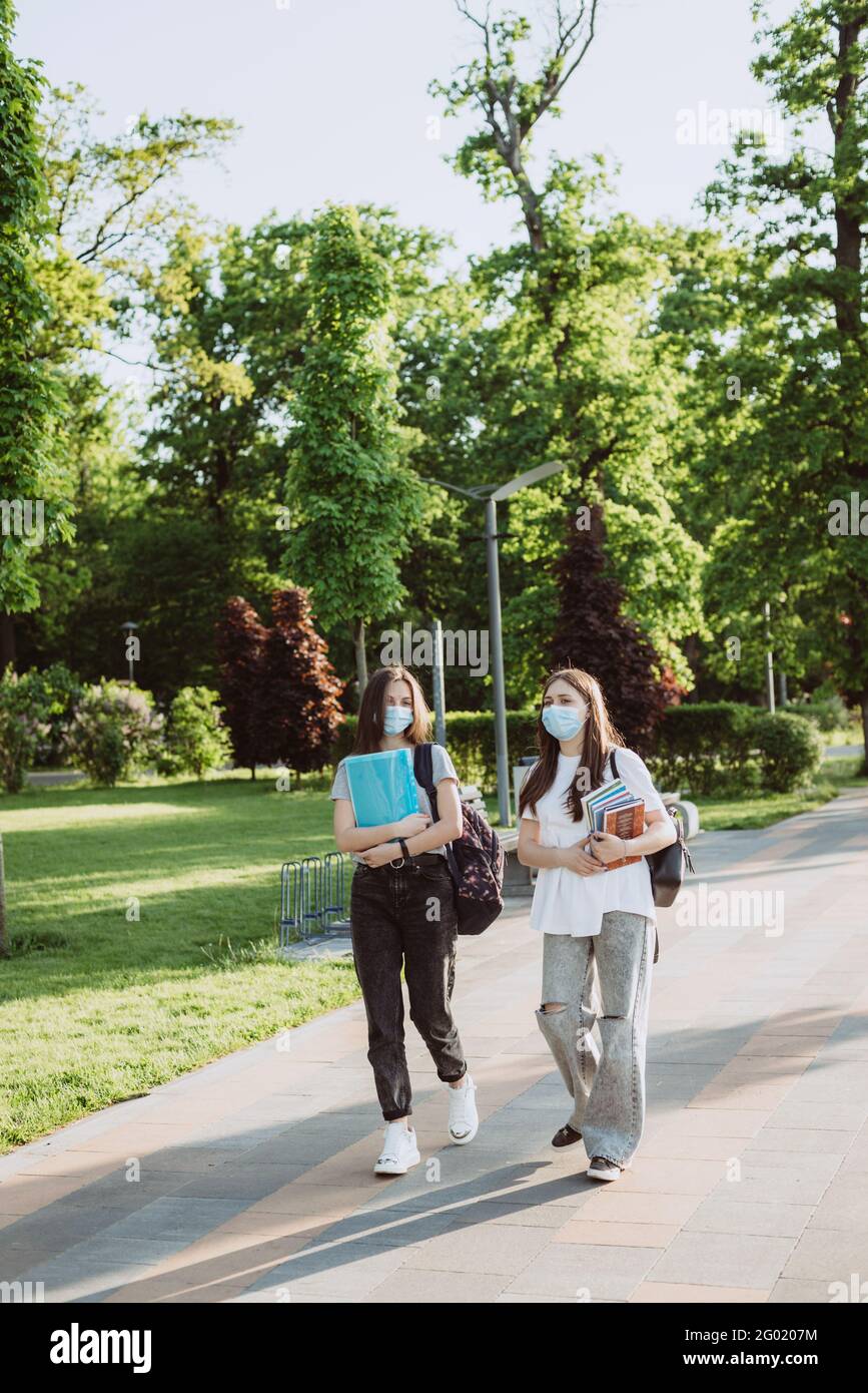 Due ragazze studentesche in maschere mediche protettive camminano e parlano nel campus. Formazione a distanza. Messa a fuoco selettiva morbida. Foto Stock