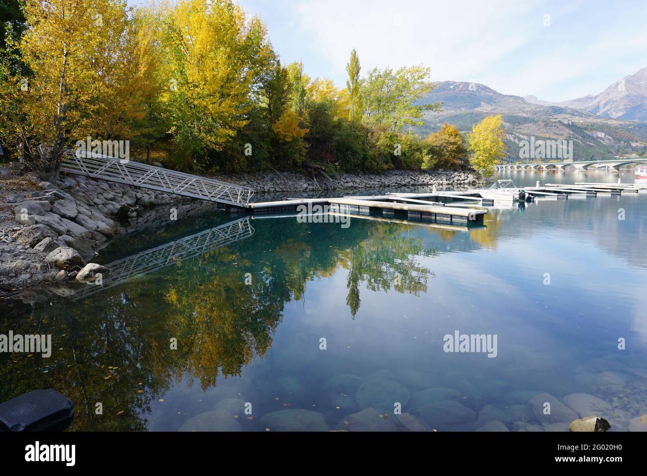 Vista panoramica del lago Serre Ponçon, Francia in un giorno d'autunno con riflesso specchio nell'acqua degli alberi e molo nel porto Foto Stock