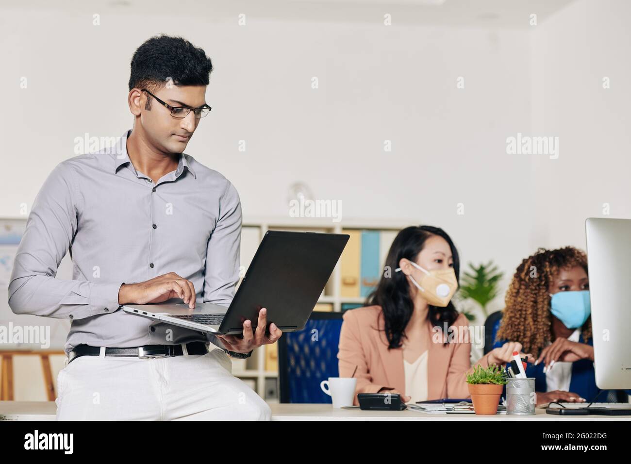 Sviluppatore di software intelligente sicuro che si appoggia al tavolo da ufficio e lavora su un computer portatile Foto Stock