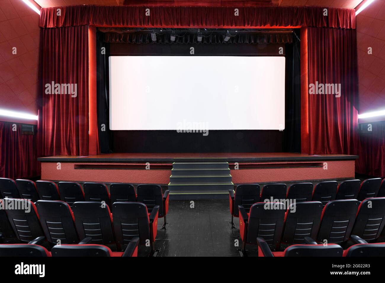 Schermo bianco vuoto nel cinema vuoto con righe di sedili e interni rossi Foto Stock