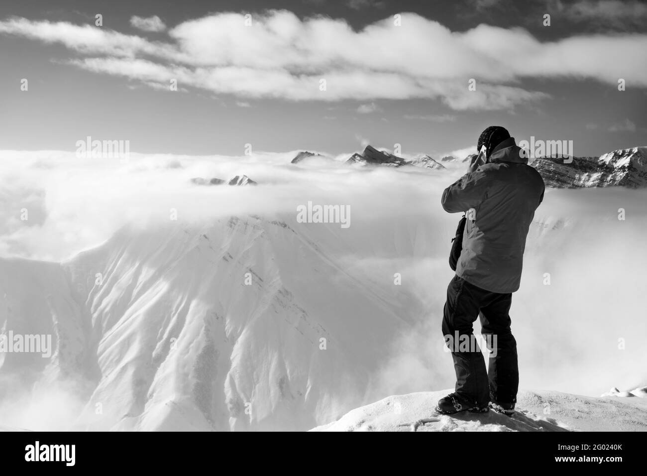 Sciatore in cima al monte alto che parla sul cellulare e sulle montagne innevate nella nebbia. Montagne del Caucaso in sole giorno d'inverno, Georgia, regione Gudauri. Nero e w Foto Stock