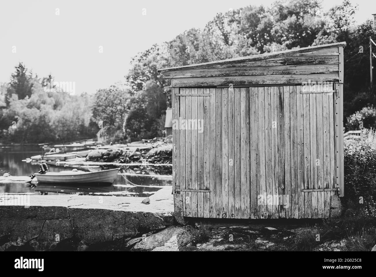 Vecchio capannone di legno, barca e molo sul fiume in scala di grigi Foto Stock