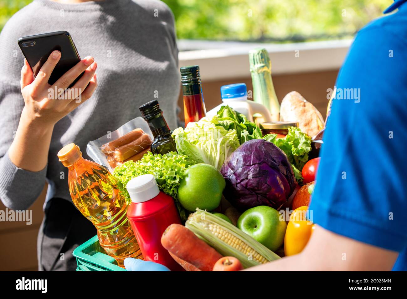 Addetto alla consegna che fornisce generi alimentari che hanno ordinato online a una donna cliente a casa, servizio di consegna di cibo in tempo di concetto pandemico Foto Stock