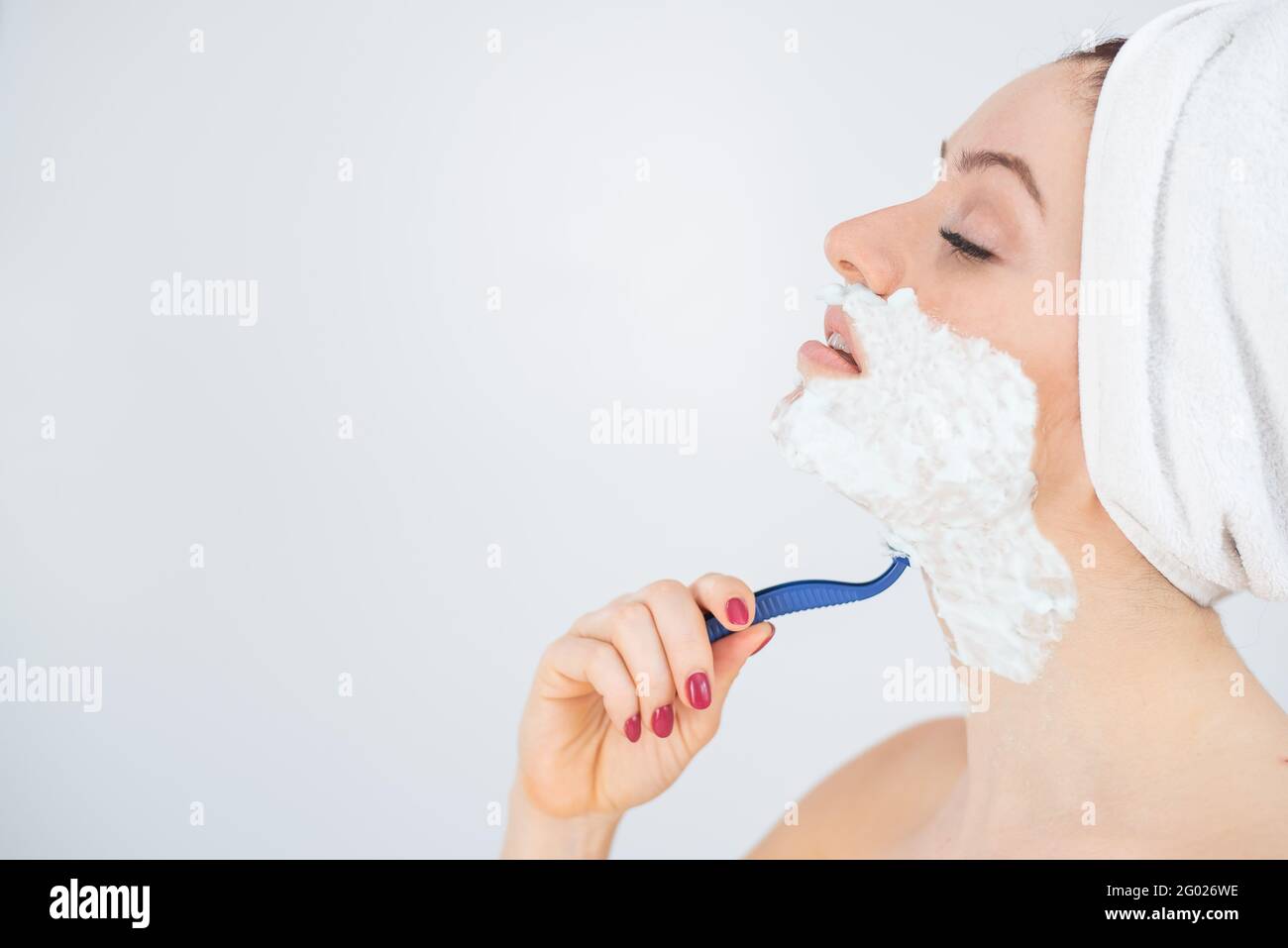 Una donna con un asciugamano di spugna bianca sulla testa e con la schiuma  da barba sul viso si rasa su sfondo bianco Foto stock - Alamy