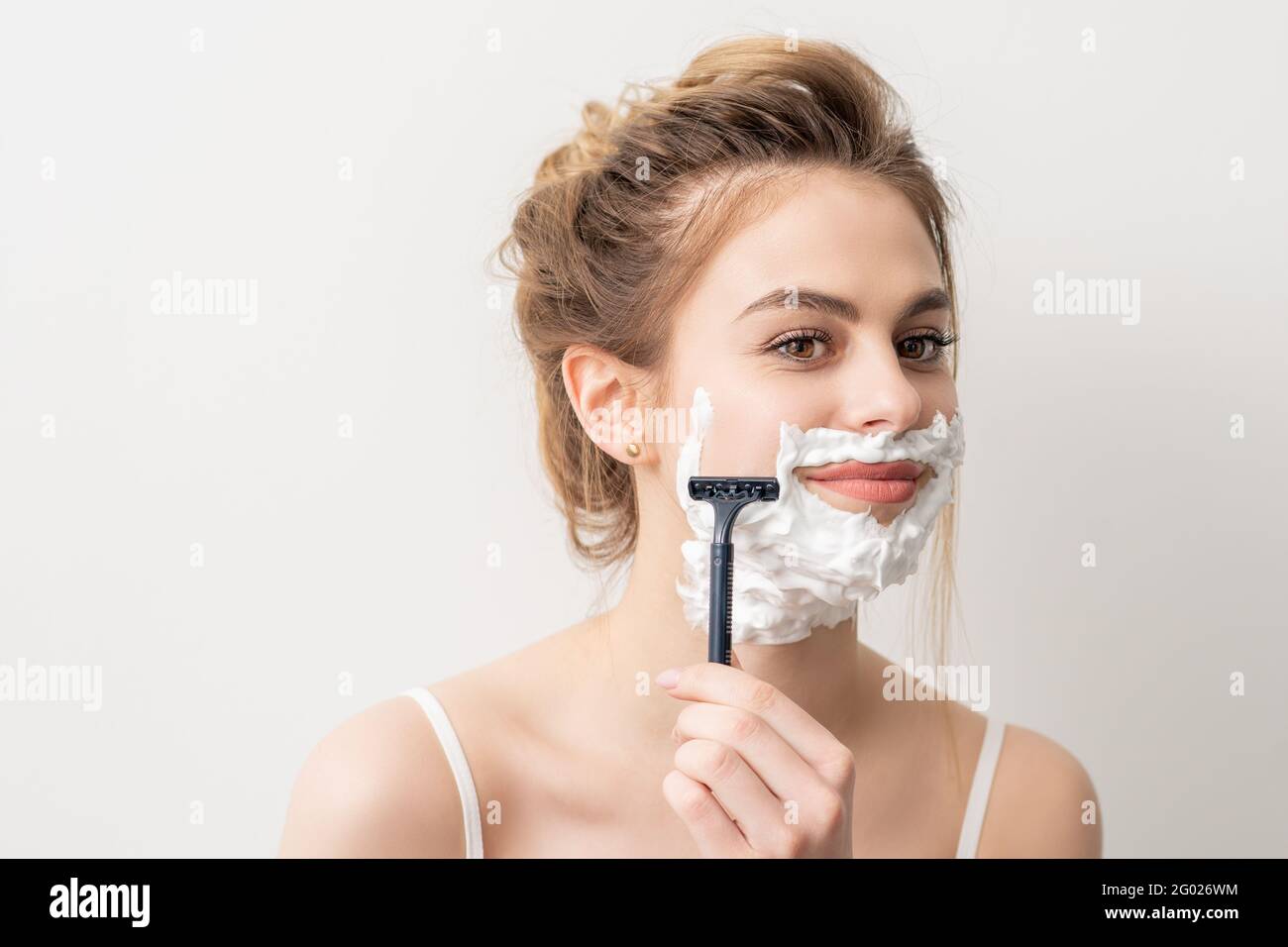 Bella giovane caucasica sorridente donna rasando il viso con rasoio su sfondo bianco Foto Stock