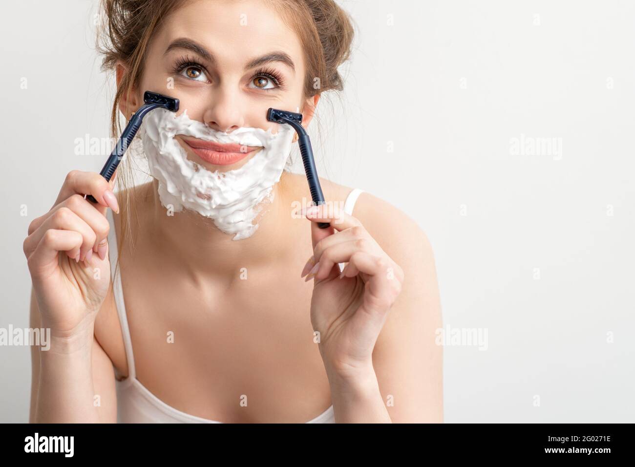 Bella giovane caucasica sorridente donna rasando il viso con rasoio guardando su sfondo bianco Foto Stock