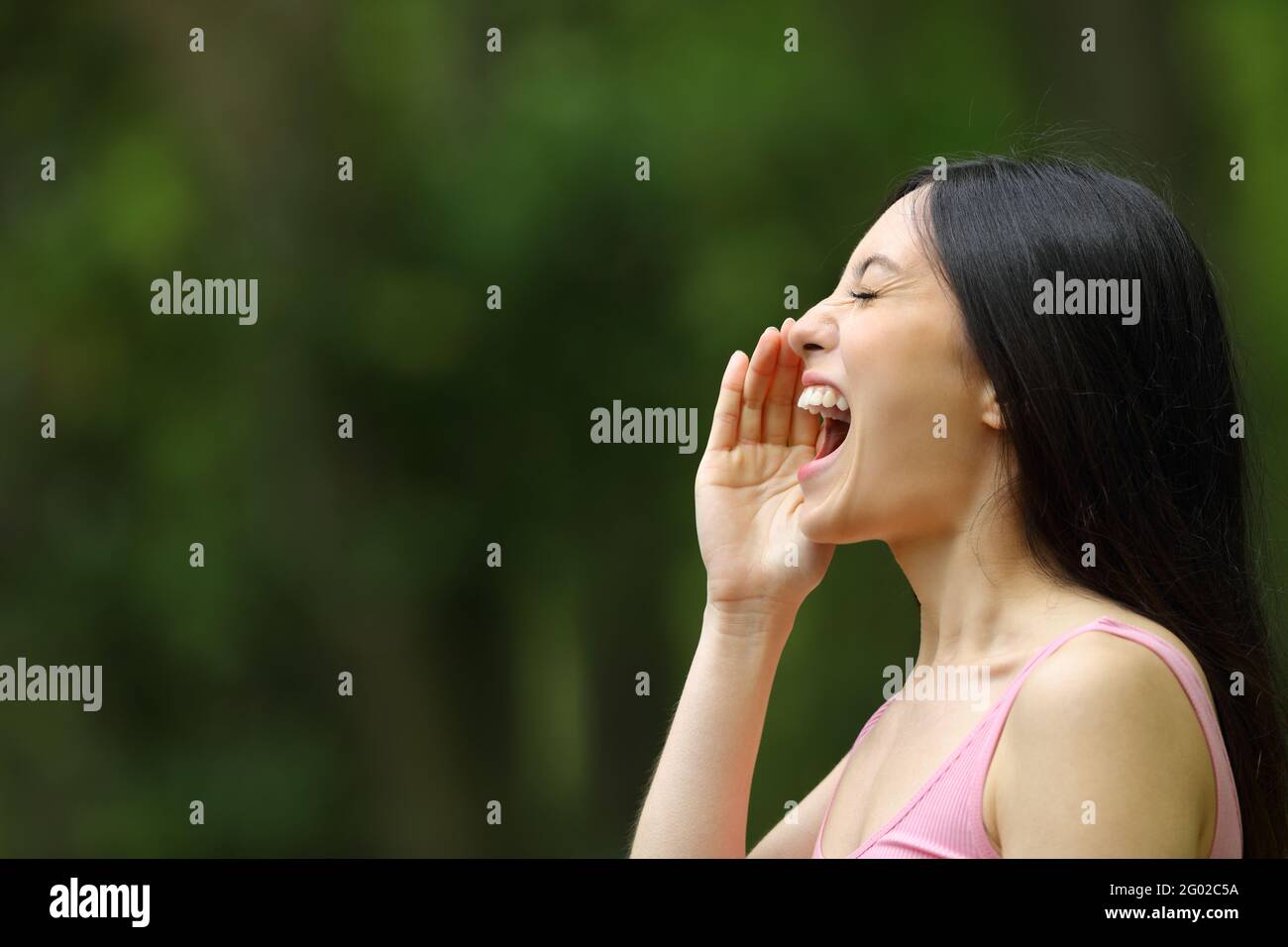 Profilo di una donna asiatica gridando con la mano sulla bocca in un parco Foto Stock