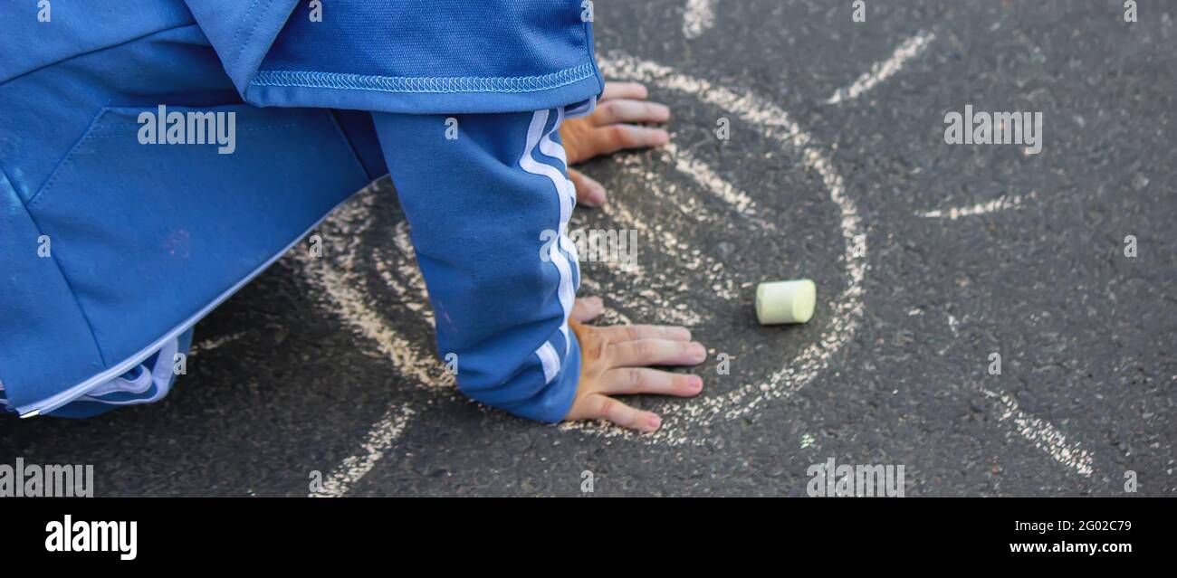 Carino bambino disegna il sole con gesso all'aperto, in estate, gesso. Messa a fuoco selettiva. Natura Foto Stock