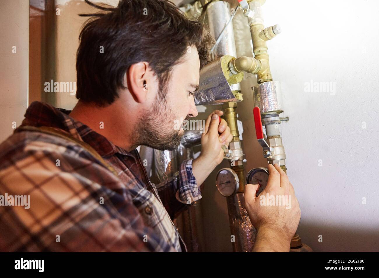 Un installatore di riscaldamento controlla il tubo dell'acqua nel seminterrato da un impianto di riscaldamento Foto Stock