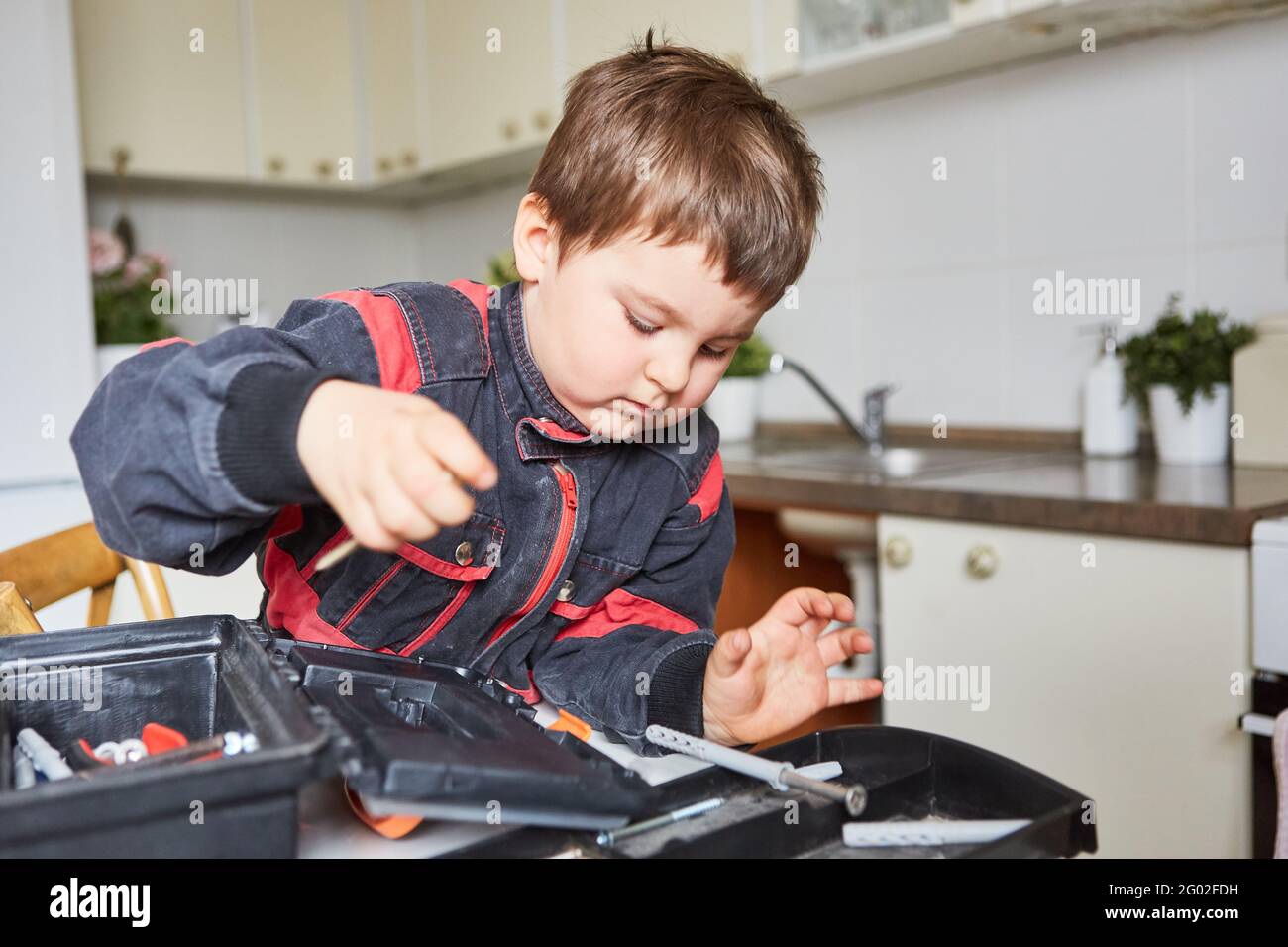 Ragazzo sta cercando gli attrezzi nella cassetta degli attrezzi mentre handyman giocare in cucina Foto Stock