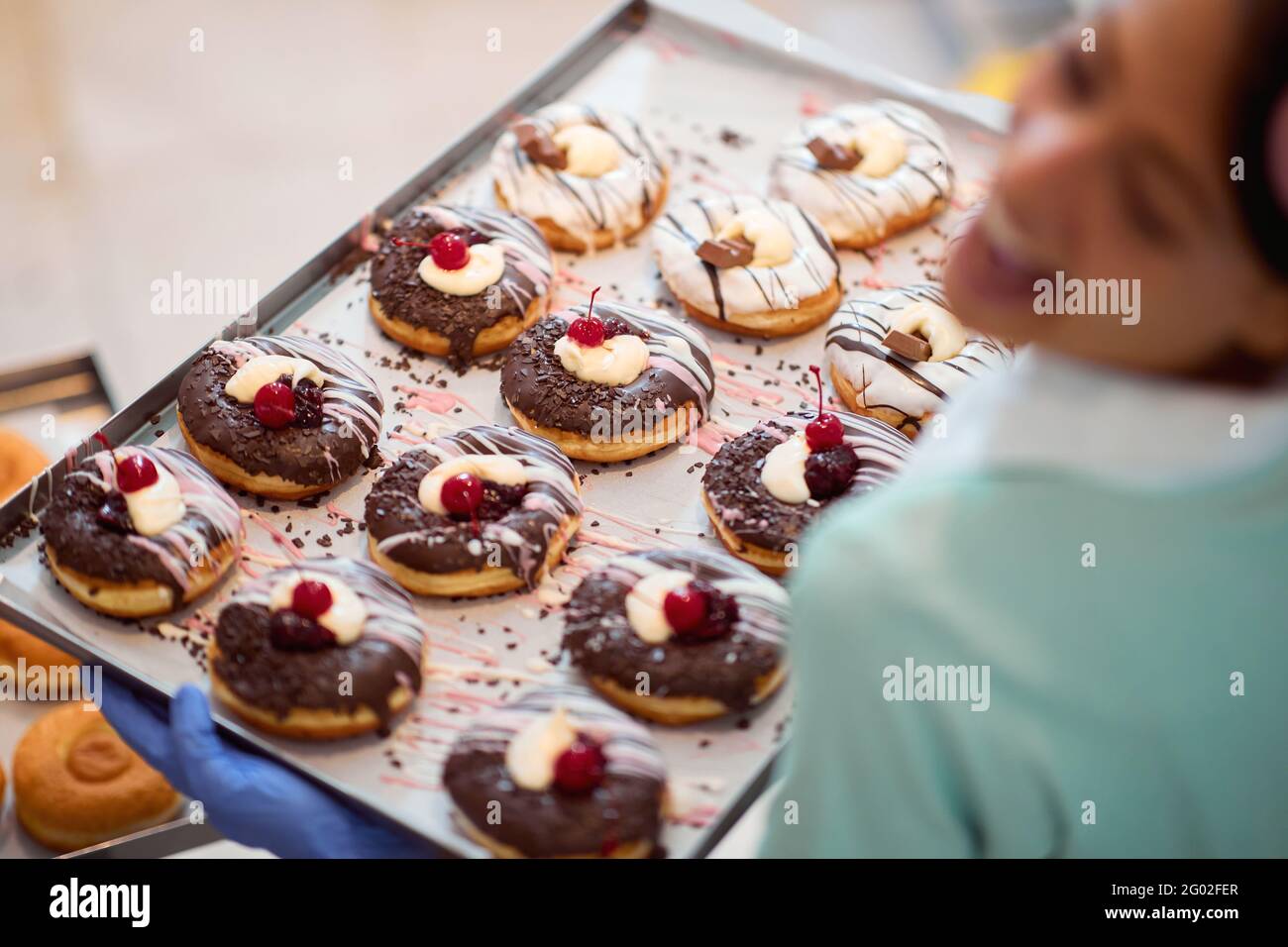 Una giovane piccola impresa donna proprietario è felice di un vassoio pieno di deliziose ciambelle fatte a mano di irresistibilità aspetto pronto per una pasticceria. Pas Foto Stock