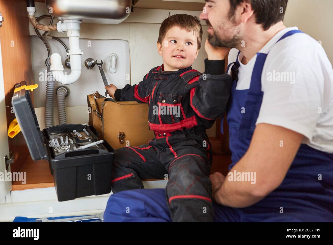 Bambino che aiuta suo padre, un handyman, a riparare il lavello in cucina Foto Stock