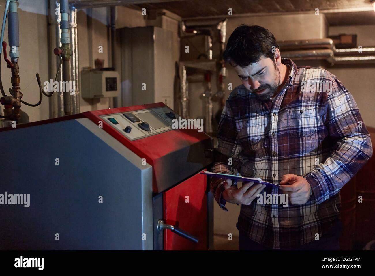 Installatore accanto al riscaldamento a gas nel seminterrato per la manutenzione della caldaia a condensazione Foto Stock