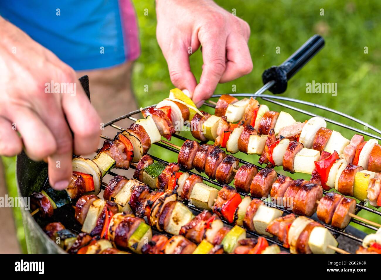 Grigliare il cibo alla griglia, preparare le mani spiedini con verdure e salsicce, festa all'aperto con barbecue sull'erba Foto Stock