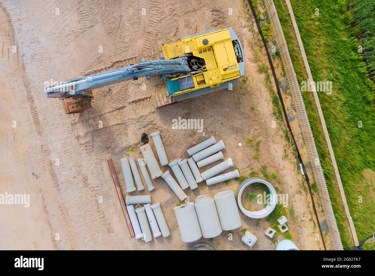 Piccolo escavatore su tubo di drenaggio in calcestruzzo impilato in cantiere Foto Stock