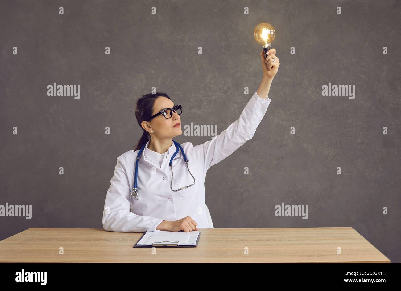 Medico o studente di medicina seduto alla scrivania e tenendo in mano la luce lampadina come concetto di idea innovativa Foto Stock