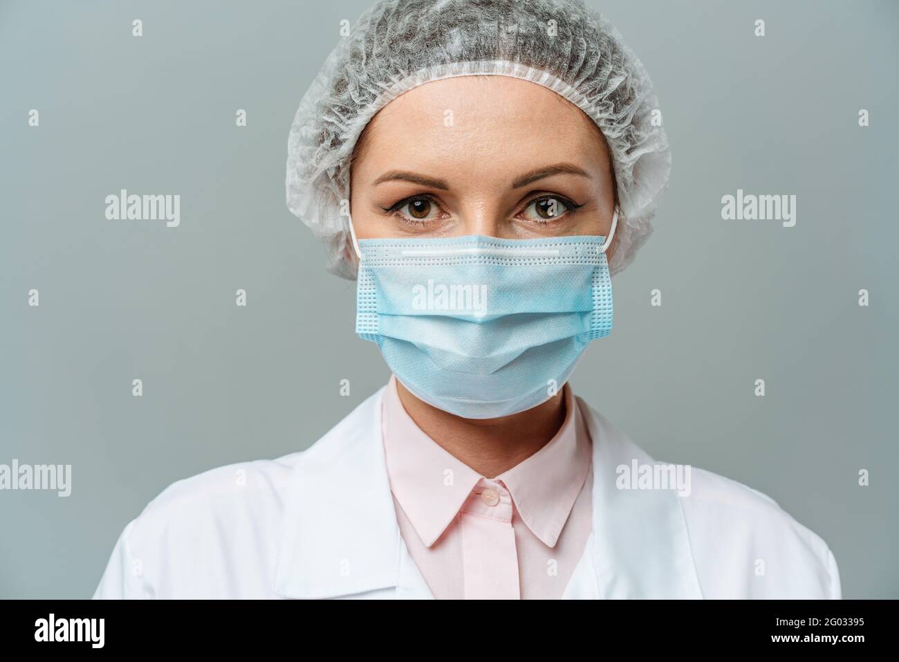 Ritratto di una giovane donna infelice medico in una maschera medica su sfondo grigio. Gli occhi stanchi del medico. Il concetto di coronavirus. Foto Stock