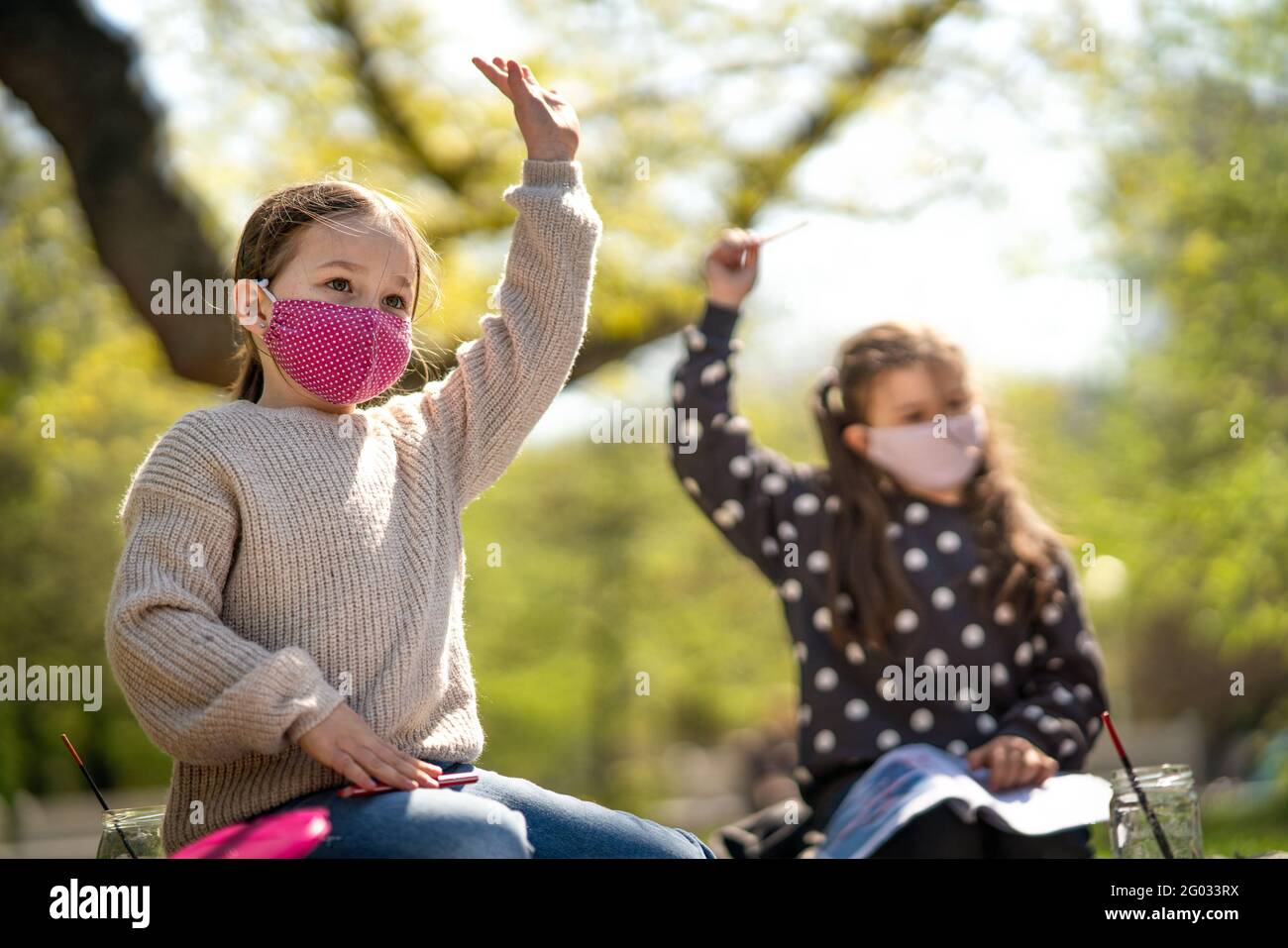 Bambini piccoli seduti all'aperto nel parco cittadino, formazione di gruppo e concetto di coronavirus. Foto Stock