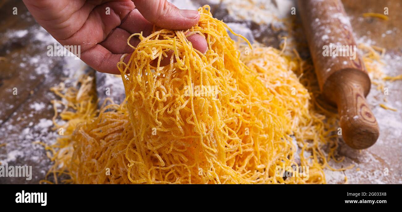 Pasta italiana all'uovo, fatta in casa e fresca su un tavolo di legno. La pasta delle tagliatelle è sottile. In mano Italiano tradizionale chiamato capelli d'angelo. Cucina rustica del nord Italia . Foto di alta qualità. Banner Foto Stock