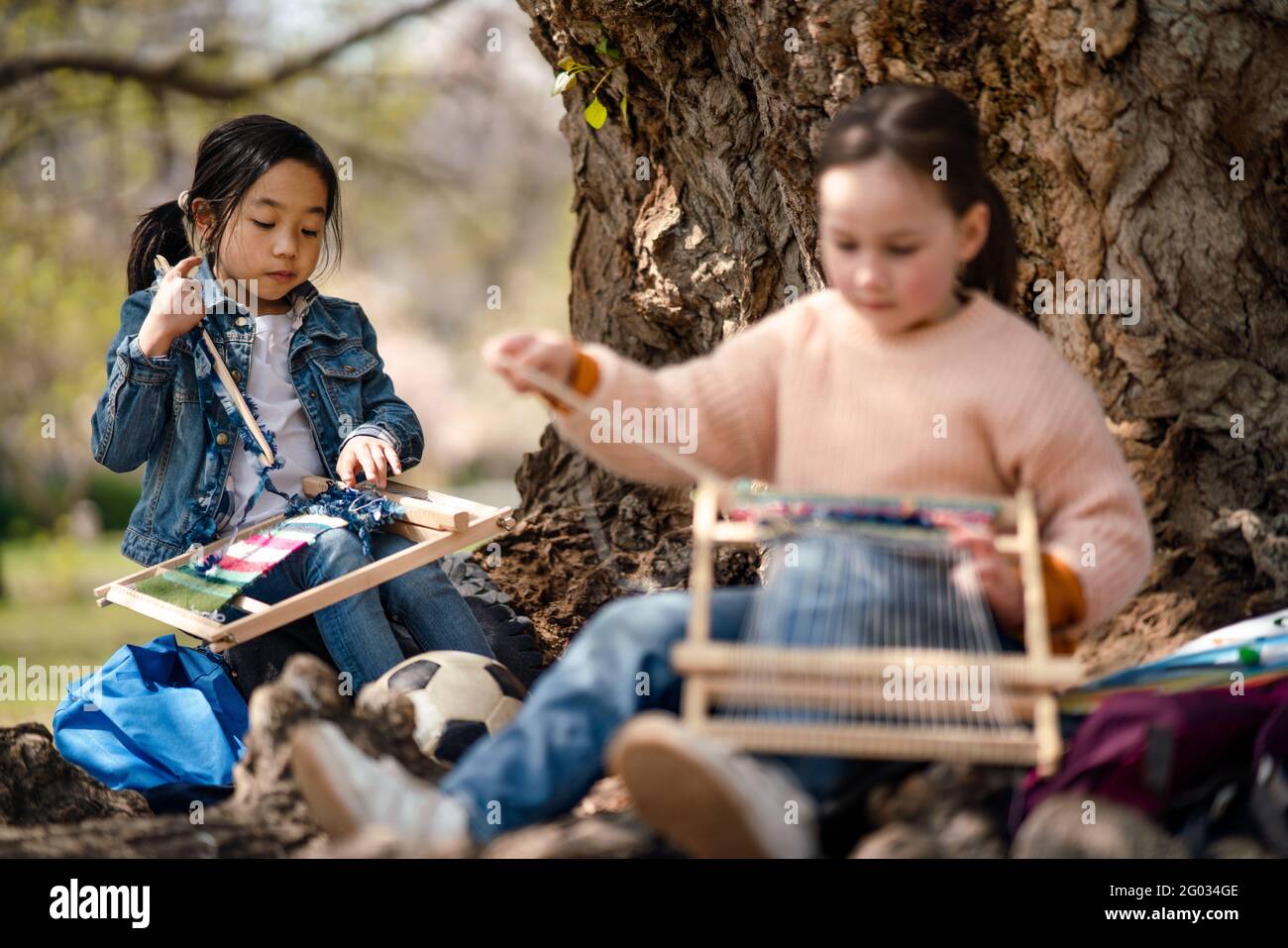 Bambini piccoli con telaio a mano seduto all'aperto nel parco cittadino, apprendimento concetto di educazione di gruppo. Foto Stock