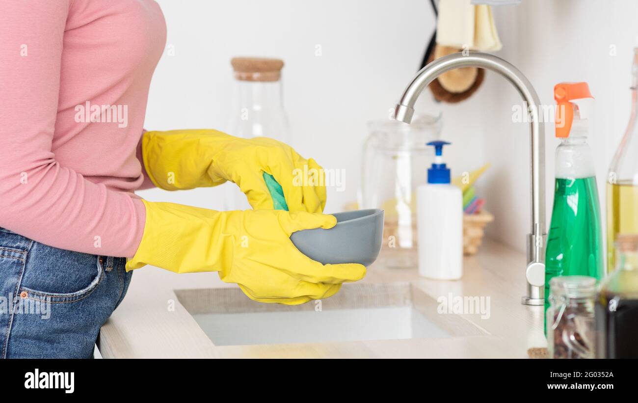 Piatti di lavaggio donna irriconoscibili, indossando guanti di gomma Foto Stock