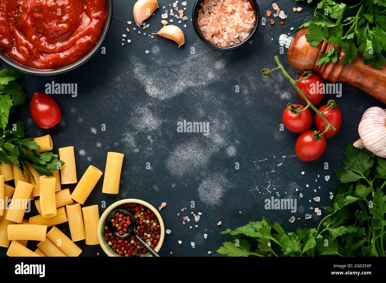 Pasta di fondo. Rigatoni di pasta, salsa di ketchup di pomodoro, olio d'oliva, spezie, prezzemolo, e pomodori freschi su un'ardesia scura, pietra o fondo di calcestruzzo. Foto Stock