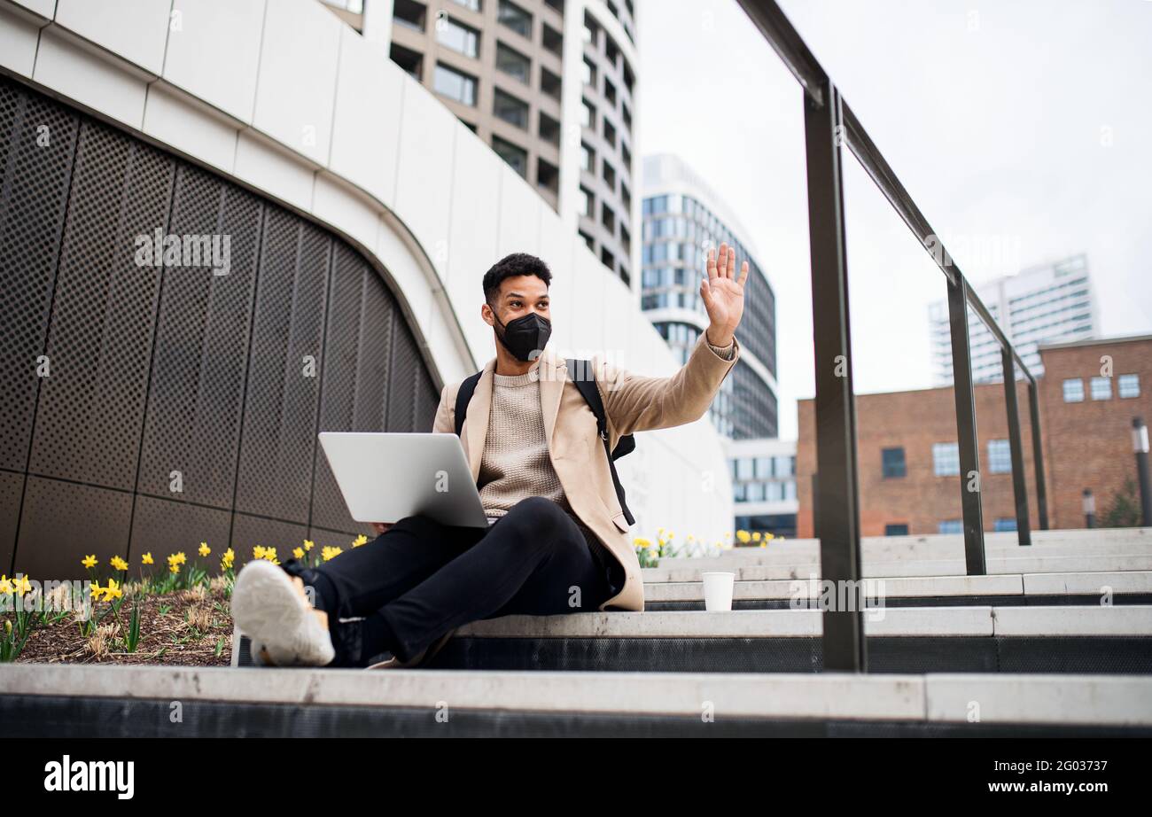 Buon uomo con un computer portatile che utilizza il computer portatile sulla strada per lavorare all'aperto in città, concetto di coronavirus. Foto Stock