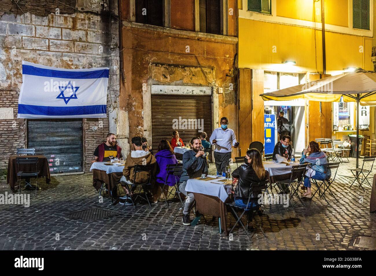 La gente cena fuori di un ristorante nel ghetto ebraico in Roma di notte  con una bandiera israeliana appesa al muro Foto stock - Alamy