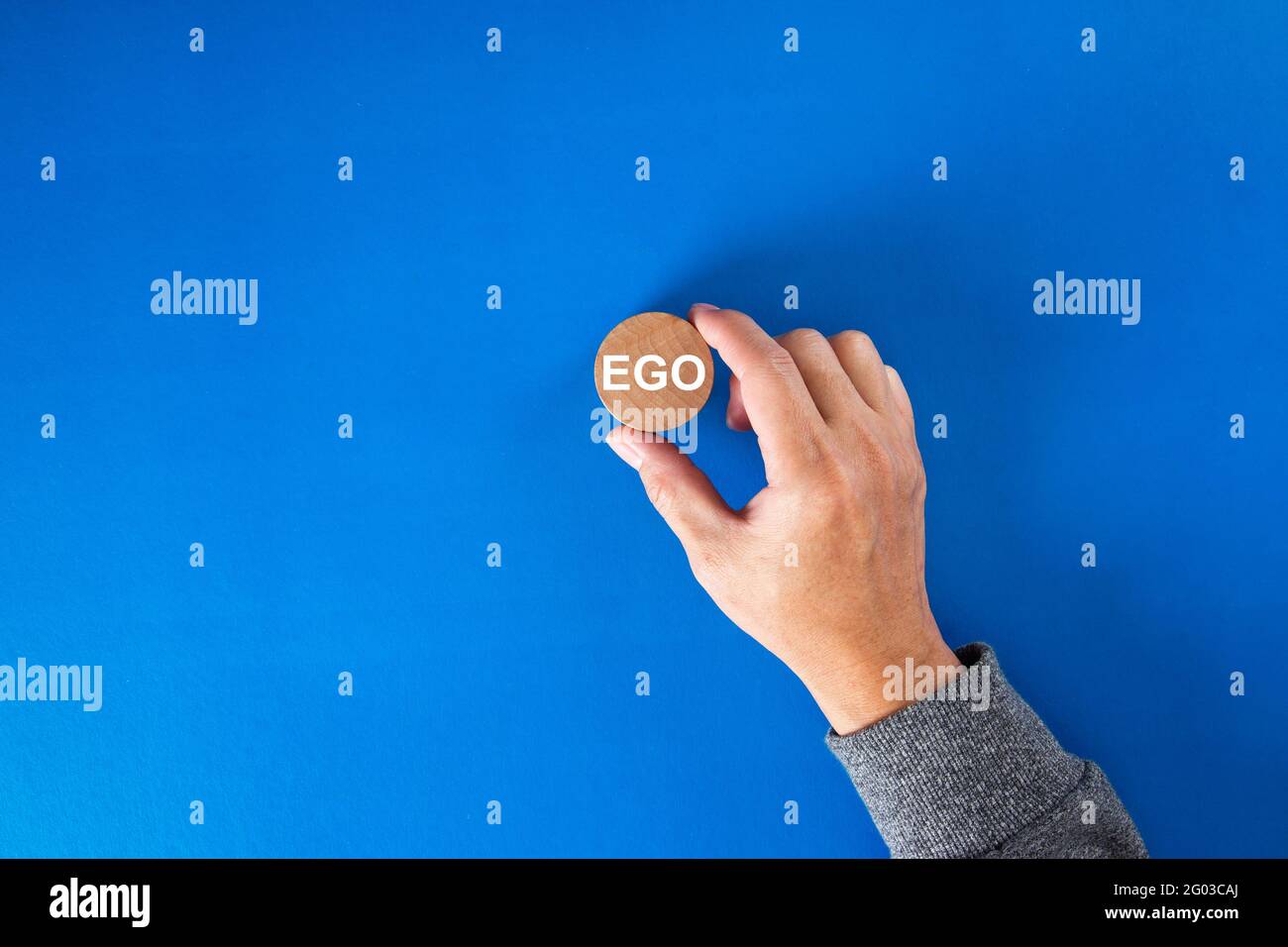 Mano dell'uomo d'affari che tiene un blocco rotondo di legno con la parola ego scritta su esso. Foto Stock